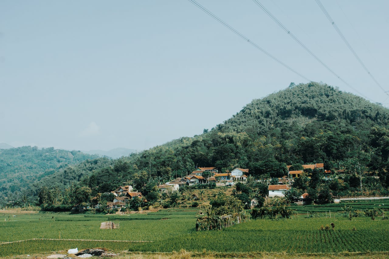 A picturesque countryside landscape of a rural village surrounded by lush greenery and rolling hills under a clear sky.